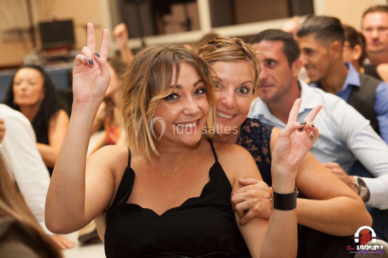 Deux femmes souriantes font un signe de paix avec leurs mains lors d'un événement festif en intérieur.