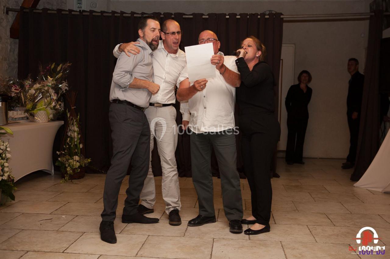 Quatre personnes chantant ensemble devant un micro dans une salle avec un rideau sombre en arrière-plan.