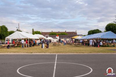 Des personnes dansent en ligne dans une salle décorée de ballons, avec des tables dressées et des convives en arrière-plan.