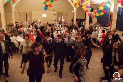 Des personnes dansent en ligne dans une salle décorée de ballons, avec des tables dressées et des convives en arrière-plan.