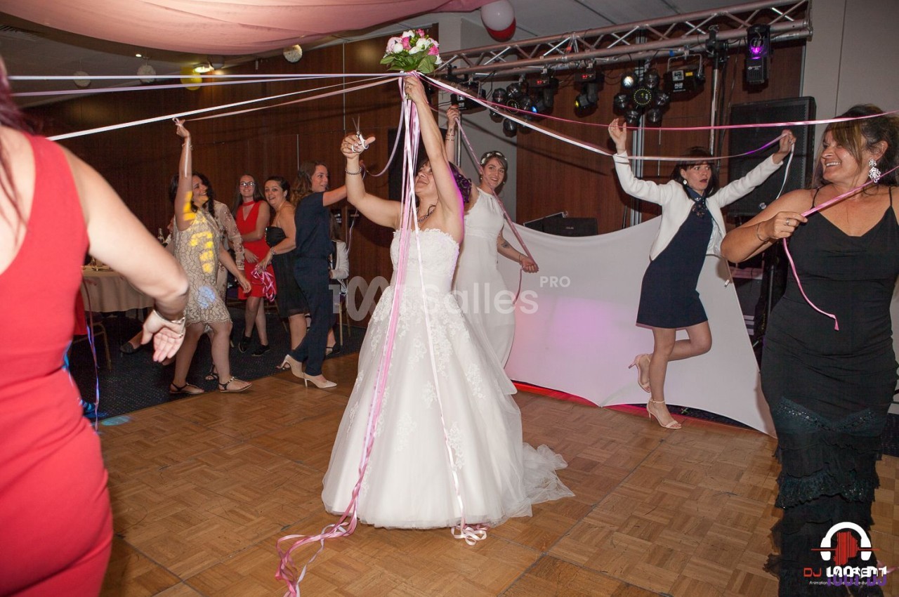 Une mariée en robe blanche participe à une danse festive avec des rubans entourée d'invités sur une piste de danse.