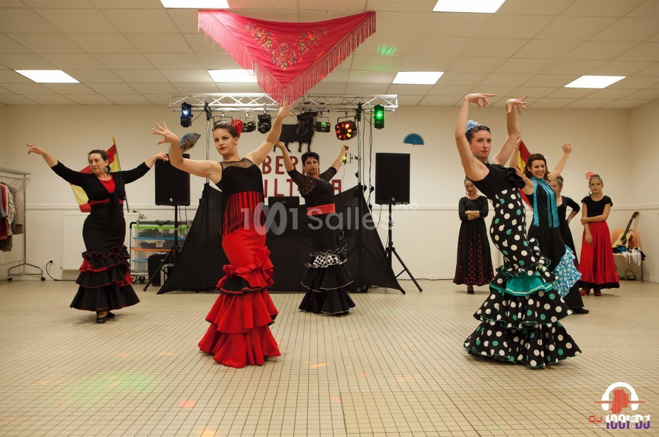 Des danseuses en tenue flamenco exécutent une chorégraphie dans une salle éclairée avec un décor de scène en arrière-plan.