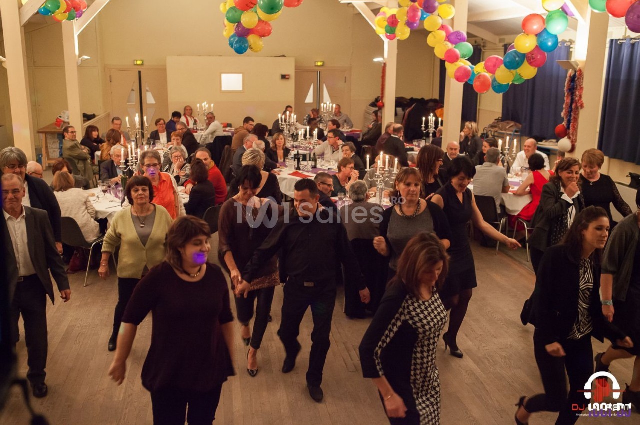 Des personnes dansent en ligne dans une salle décorée de ballons, avec des tables dressées et des convives en arrière-plan.