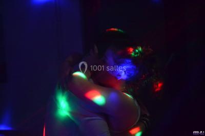 Des personnes dansent dans une ambiance festive avec des lumières colorées dans une salle sombre.