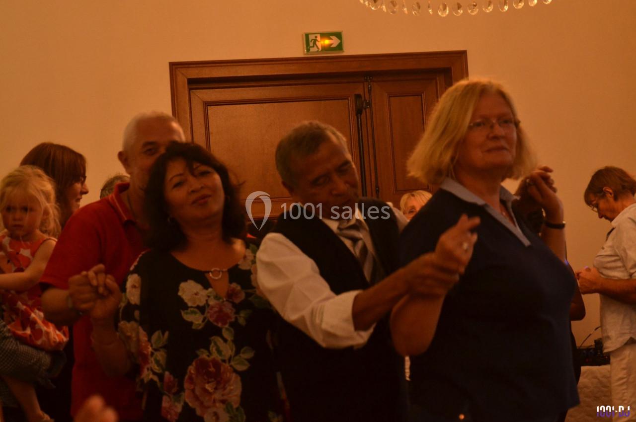 Des personnes dansent en groupe dans une salle éclairée, avec des murs clairs et une porte en bois en arrière-plan.