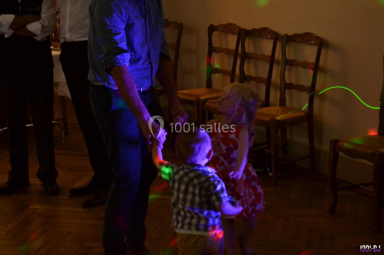 Un adulte danse avec deux jeunes enfants dans une salle éclairée par des lumières colorées.