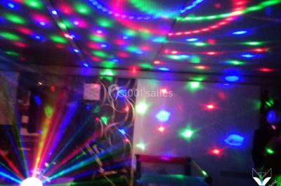 Des personnes dansent dans une ambiance festive avec des lumières colorées dans une salle sombre.