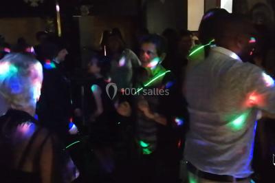 Des personnes dansent dans une ambiance festive avec des lumières colorées dans une salle sombre.