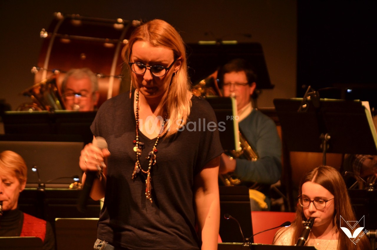 Une femme tenant un micro chante devant un orchestre en arrière-plan.
