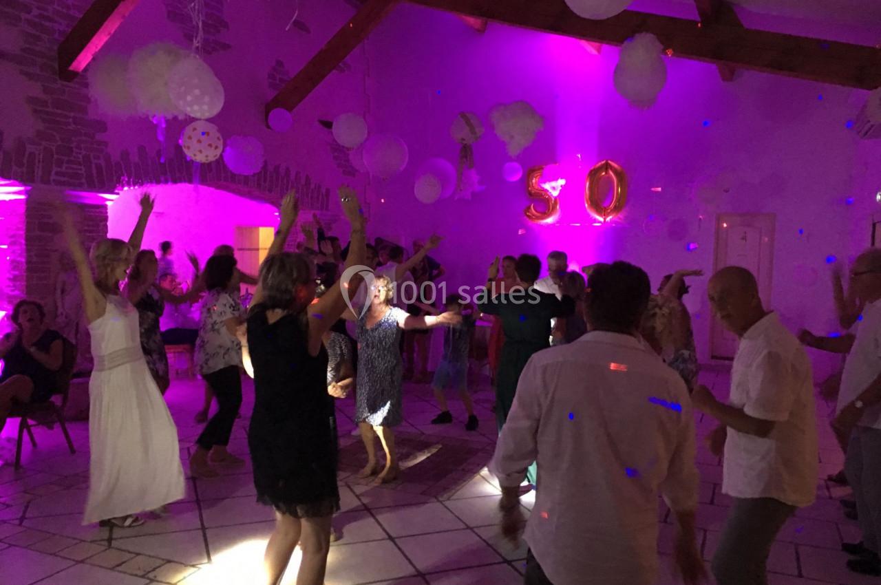 Des personnes dansent dans une salle décorée de ballons et lumières colorées lors d'une fête.