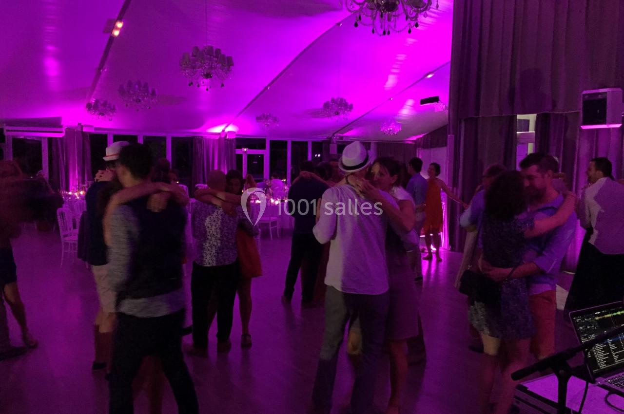 Des couples dansent dans une salle éclairée par des lumières violettes, avec des chandeliers suspendus au plafond.