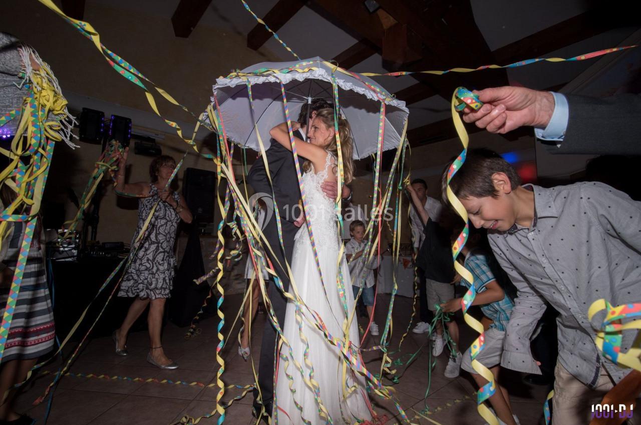 Une mariée sous un parapluie décoré entourée d'invités dansant avec des serpentins colorés.