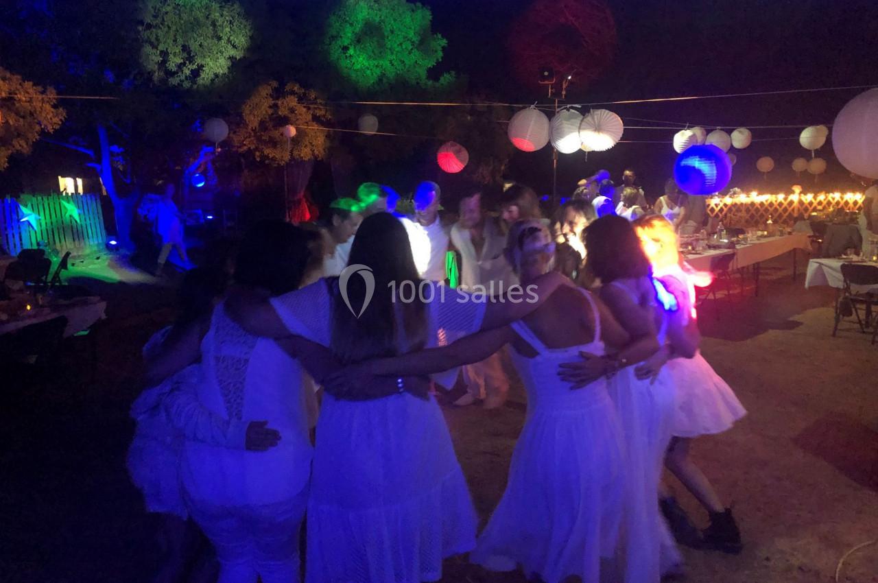 Groupe de personnes en cercle dansant sous des lumières colorées lors d'une fête en plein air, de nuit.