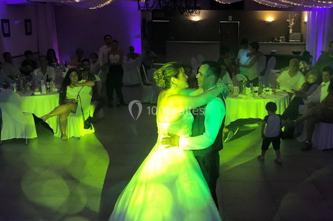 Un couple danse sous des lumières colorées dans une salle décorée pour une réception avec des invités assis.