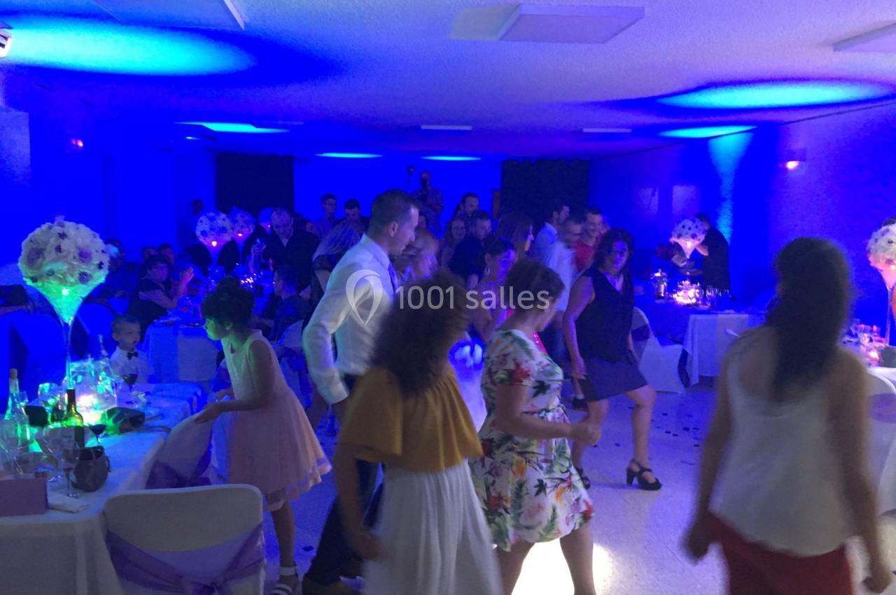 Des personnes dansent dans une salle de réception éclairée par des lumières bleues, entourées de tables décorées.