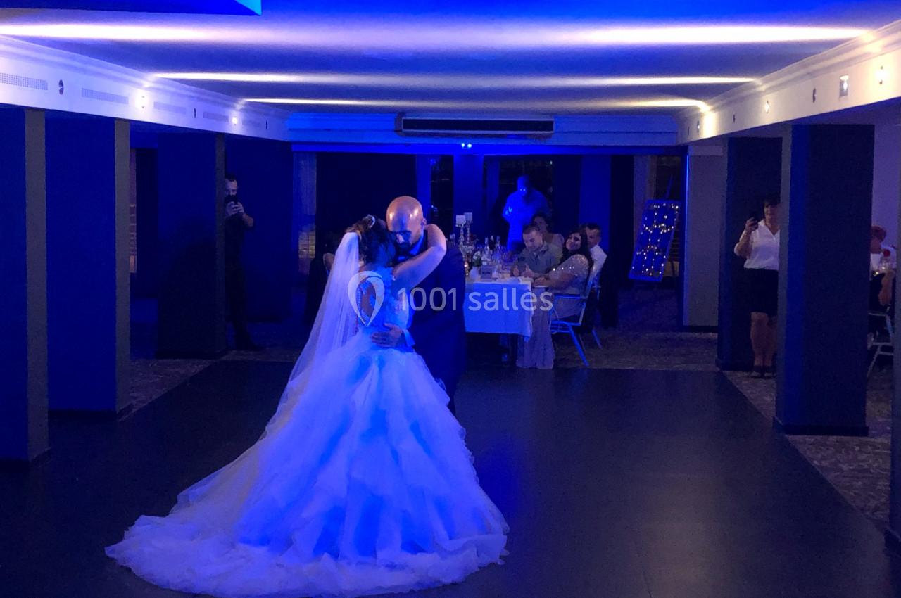 Un couple danse sous une lumière bleue dans une salle de réception, entouré de quelques invités assis.
