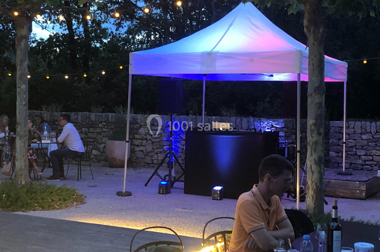 Tente blanche éclairée avec une table de DJ, installée en extérieur sous des guirlandes lumineuses au crépuscule.