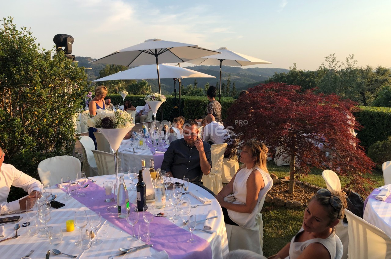Des convives assis à des tables décorées en extérieur, sous des parasols, avec un paysage vallonné en arrière-plan.