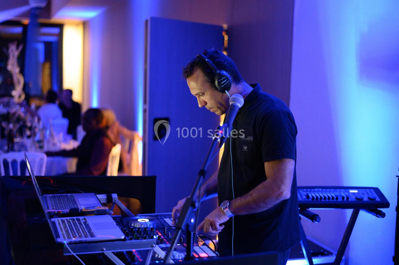 Un DJ mixant de la musique sur une console, entouré d'équipements audio, dans une salle éclairée en bleu.