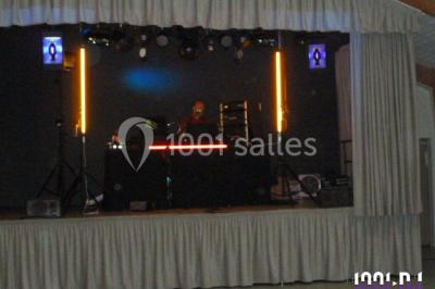 Miniature DJ Buchy (Seine-Maritime) - Djmanfred - Animmix #5 Homme souriant debout devant un micro, portant une chemise noire avec un gilet rayé, fond marron.