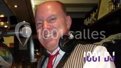 Homme souriant portant un casque audio autour du cou, debout devant un micro dans un environnement de bar.