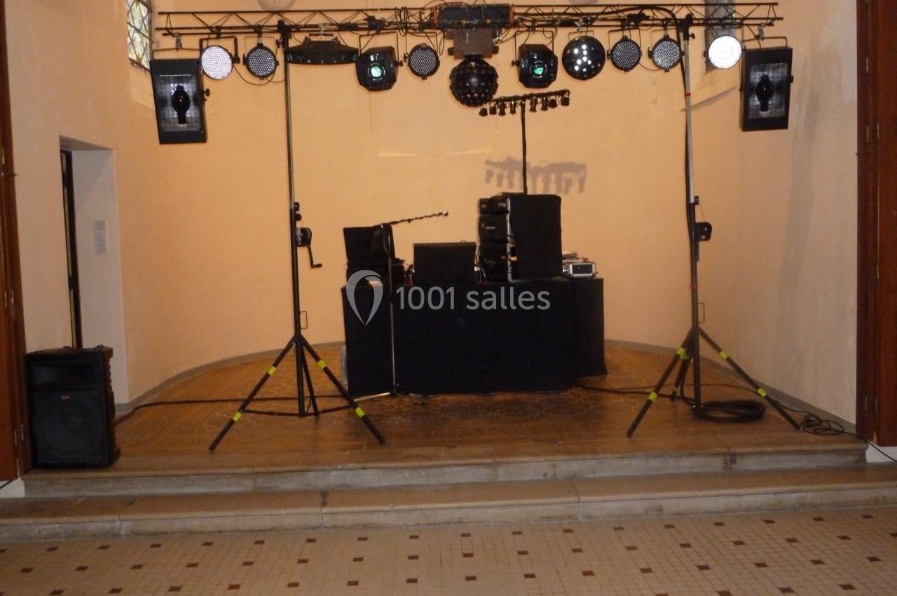 Installation de matériel de sonorisation et d'éclairage sur une scène dans une salle aux murs clairs.