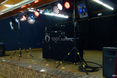 Miniature DJ Buchy (Seine-Maritime) - Djmanfred - Animmix #17 Homme souriant debout devant un micro, portant une chemise noire avec un gilet rayé, fond marron.