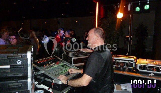 Un DJ mixe de la musique sur une console dans une salle animée avec des lumières et des invités dansant en arrière-plan.