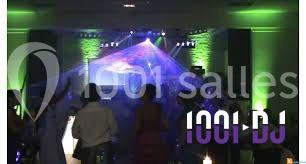 Miniature DJ Buchy (Seine-Maritime) - Djmanfred - Animmix #9 Homme souriant debout devant un micro, portant une chemise noire avec un gilet rayé, fond marron.