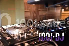 Miniature DJ Buchy (Seine-Maritime) - Djmanfred - Animmix #10 Homme souriant debout devant un micro, portant une chemise noire avec un gilet rayé, fond marron.