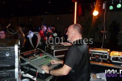 Miniature DJ Buchy (Seine-Maritime) - Djmanfred - Animmix #2 Homme souriant debout devant un micro, portant une chemise noire avec un gilet rayé, fond marron.