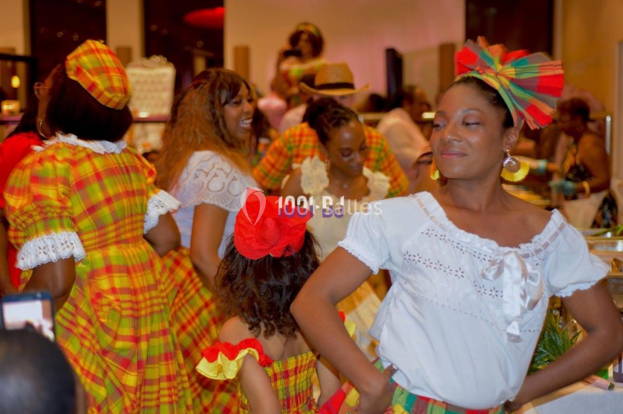 Des femmes et une enfant en tenues traditionnelles colorées dansent lors d'un événement festif en intérieur.