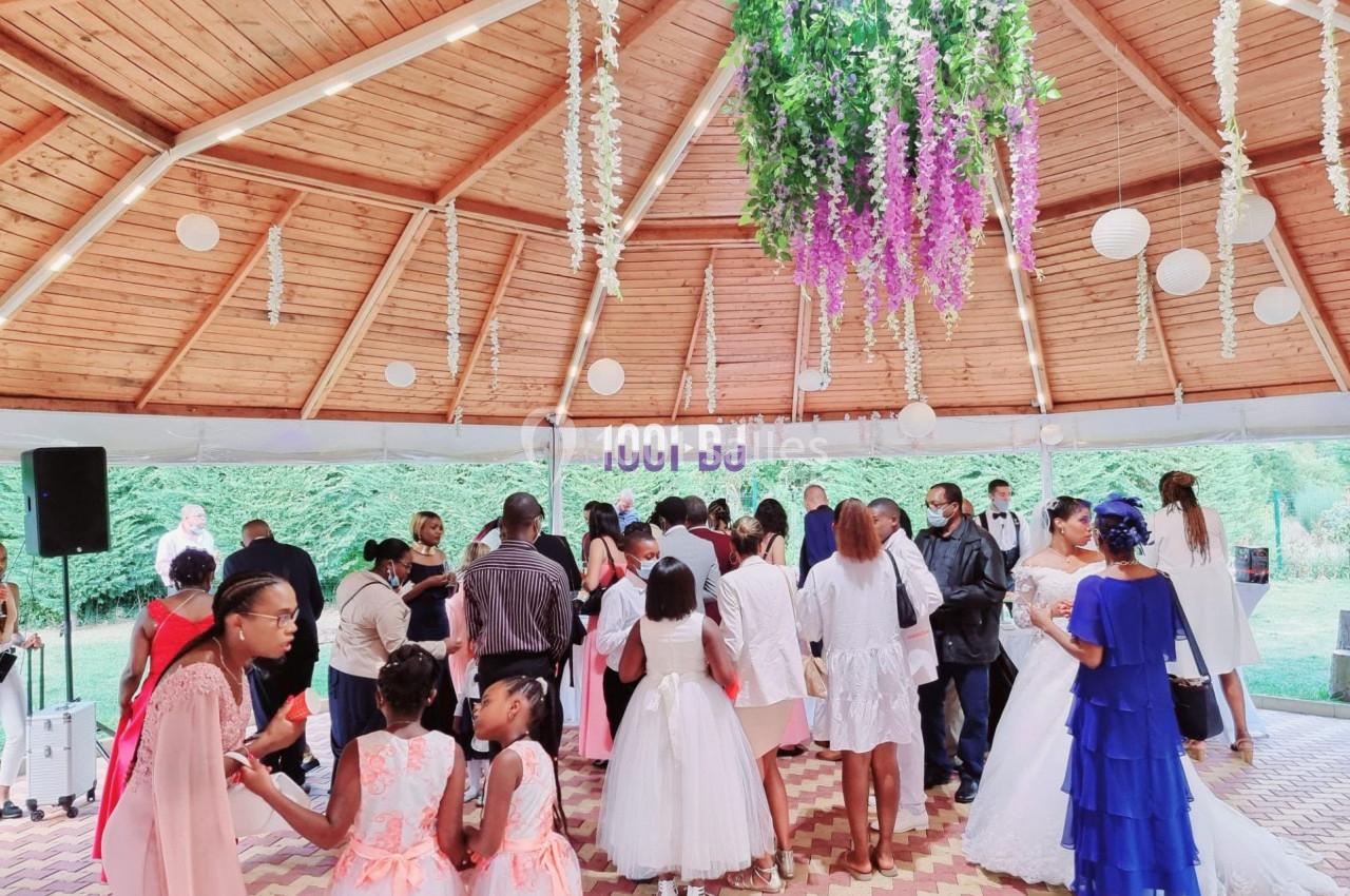 Des invités en tenue élégante discutent sous une structure en bois décorée de fleurs suspendues lors d'une réception.