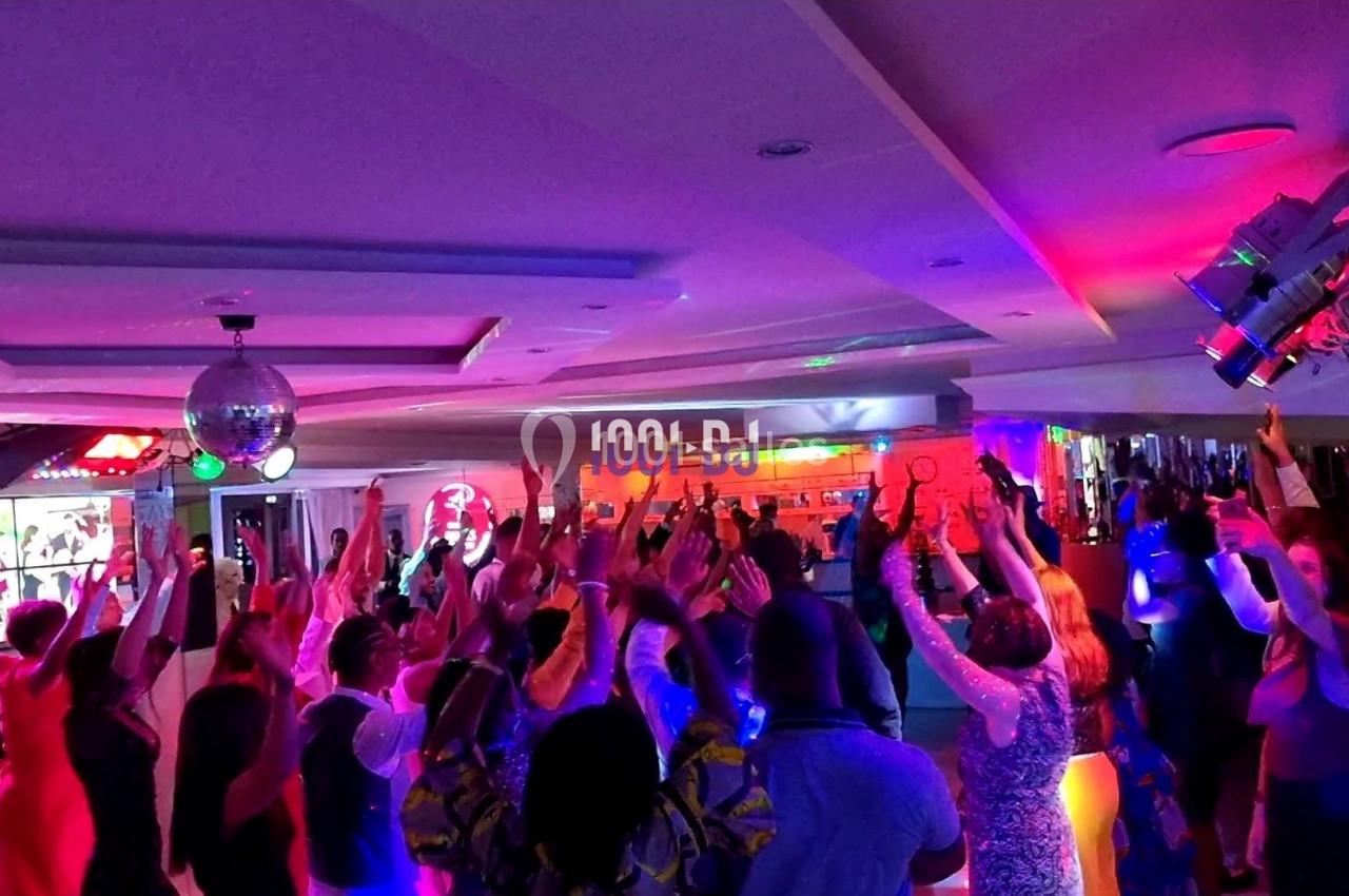 Des personnes dansent sous des lumières colorées dans une salle festive avec une boule disco suspendue.