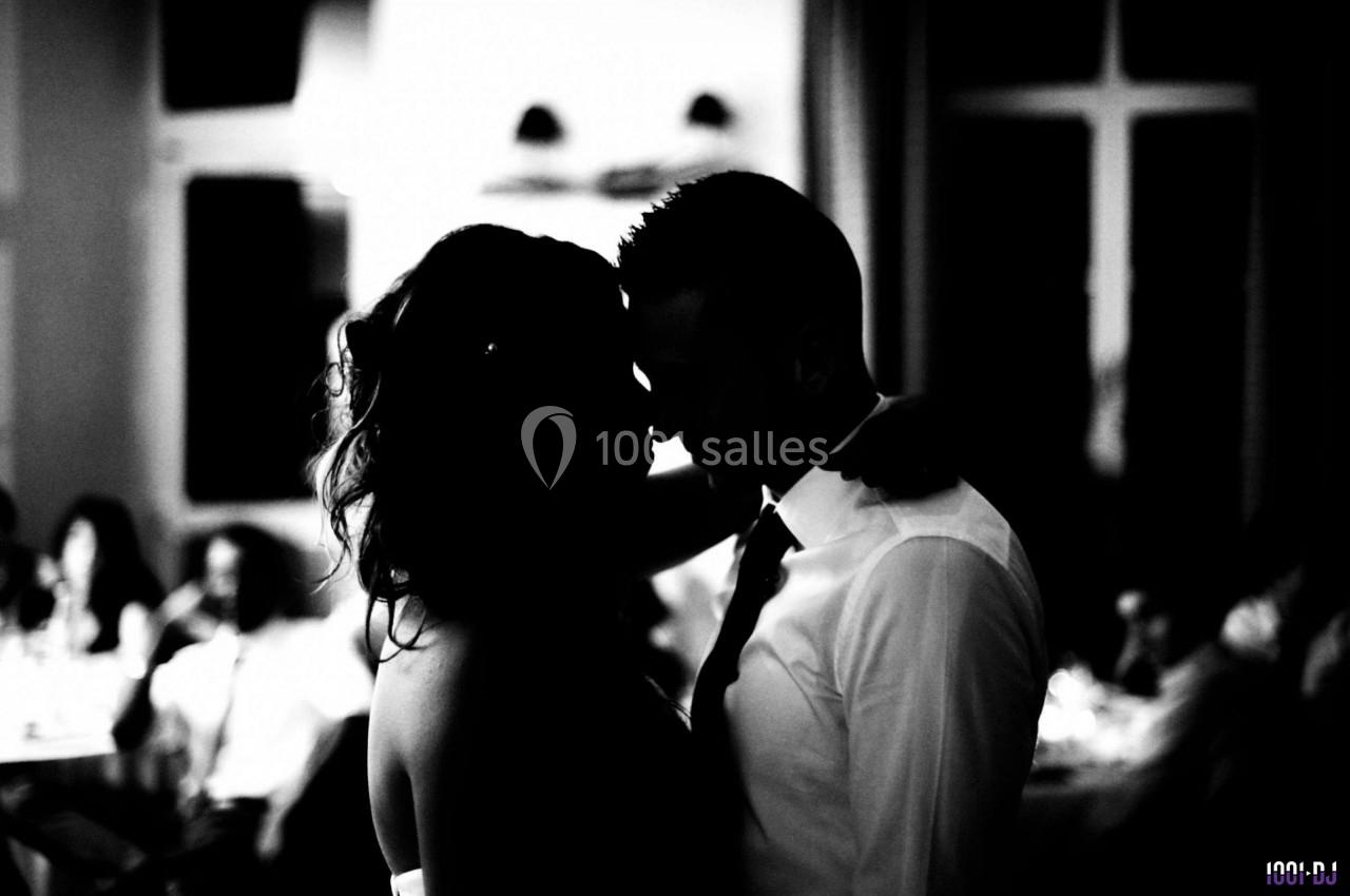 Un couple dansant en silhouette dans une ambiance tamisée, entouré de convives flous en arrière-plan.