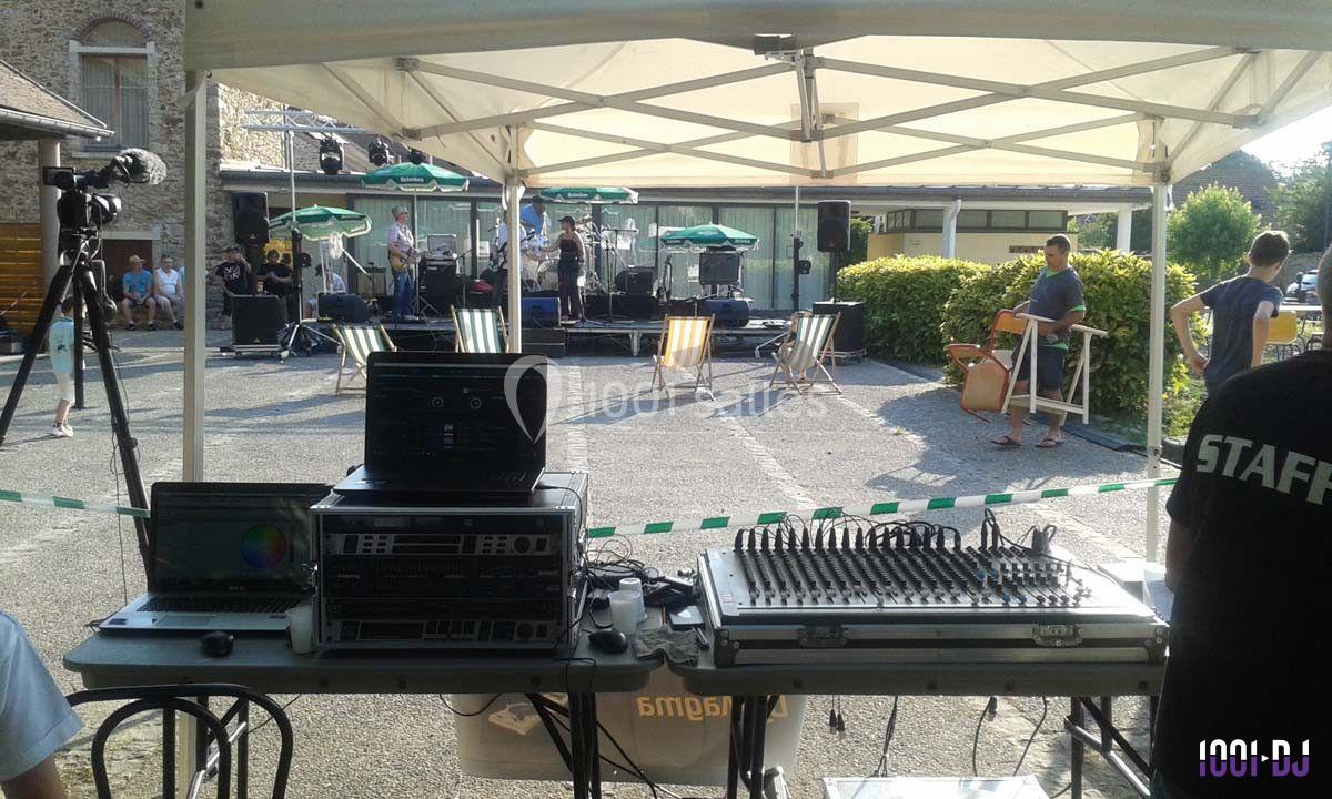 Matériel de sonorisation installé sous un barnum, avec une scène en arrière-plan et des spectateurs en extérieur.