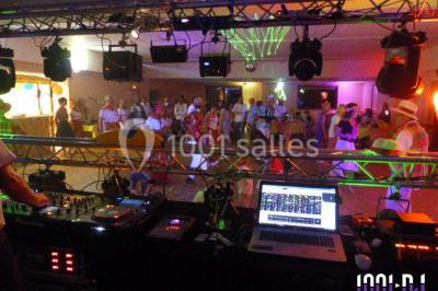 Salle de réception décorée avec des tables dressées, nappes blanches, chaises houssées et arrangements floraux.