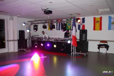 Salle de réception décorée avec des tables dressées, nappes blanches, chaises houssées et arrangements floraux.