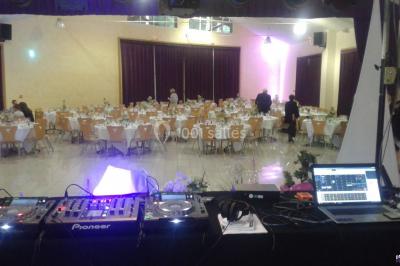 Salle de réception décorée avec des tables dressées, nappes blanches, chaises houssées et arrangements floraux.
