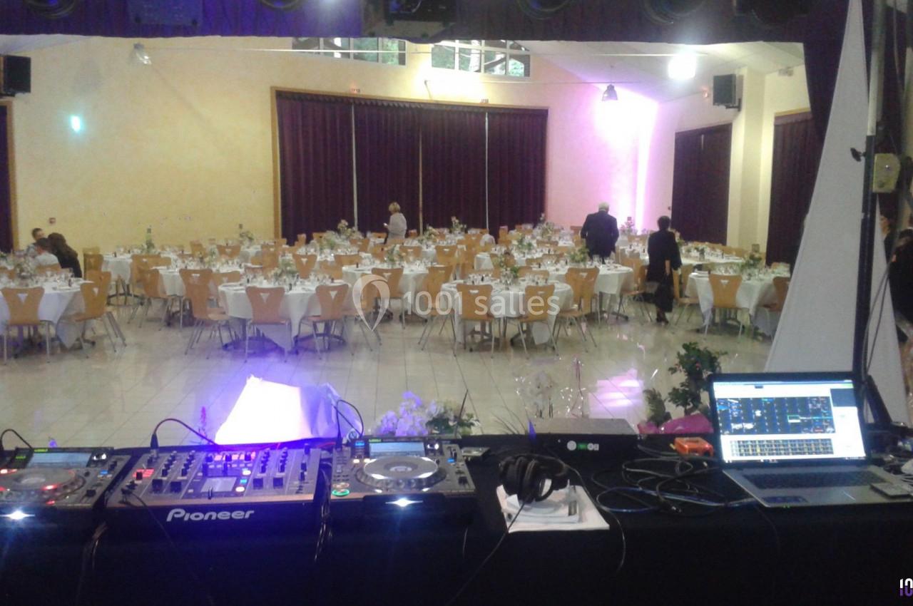 Salle de réception avec tables dressées pour un événement, vue depuis une table de mixage avec équipements DJ.