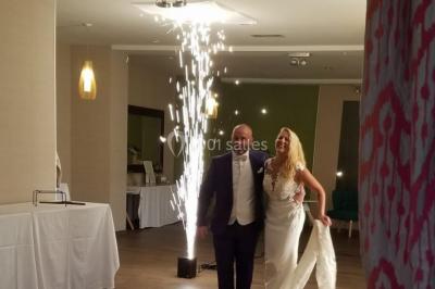 Salle de réception décorée avec des tables dressées, nappes blanches, chaises houssées et arrangements floraux.