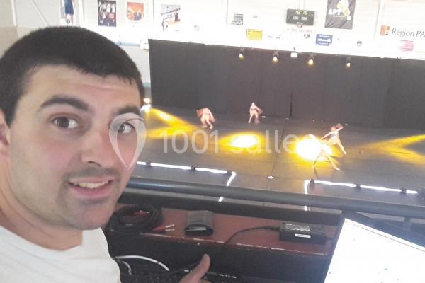 Homme souriant en premier plan devant une scène éclairée où des danseurs exécutent une performance.