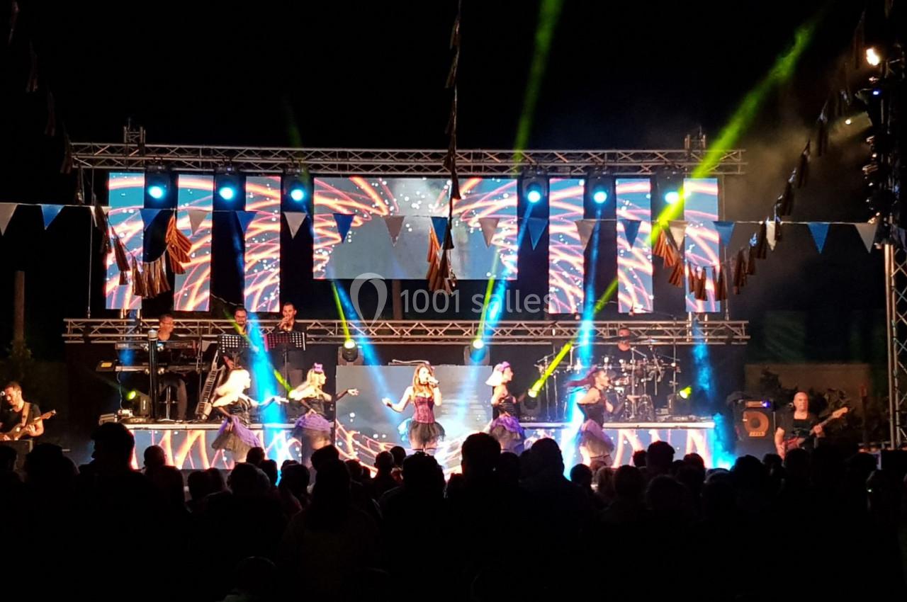 Groupe musical se produisant sur une scène illuminée avec des jeux de lumière et un public en contre-jour.