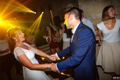 Salle avec éclairage de scène coloré, piste de danse illuminée, tables sur les côtés et matériel audio en arrière-plan.