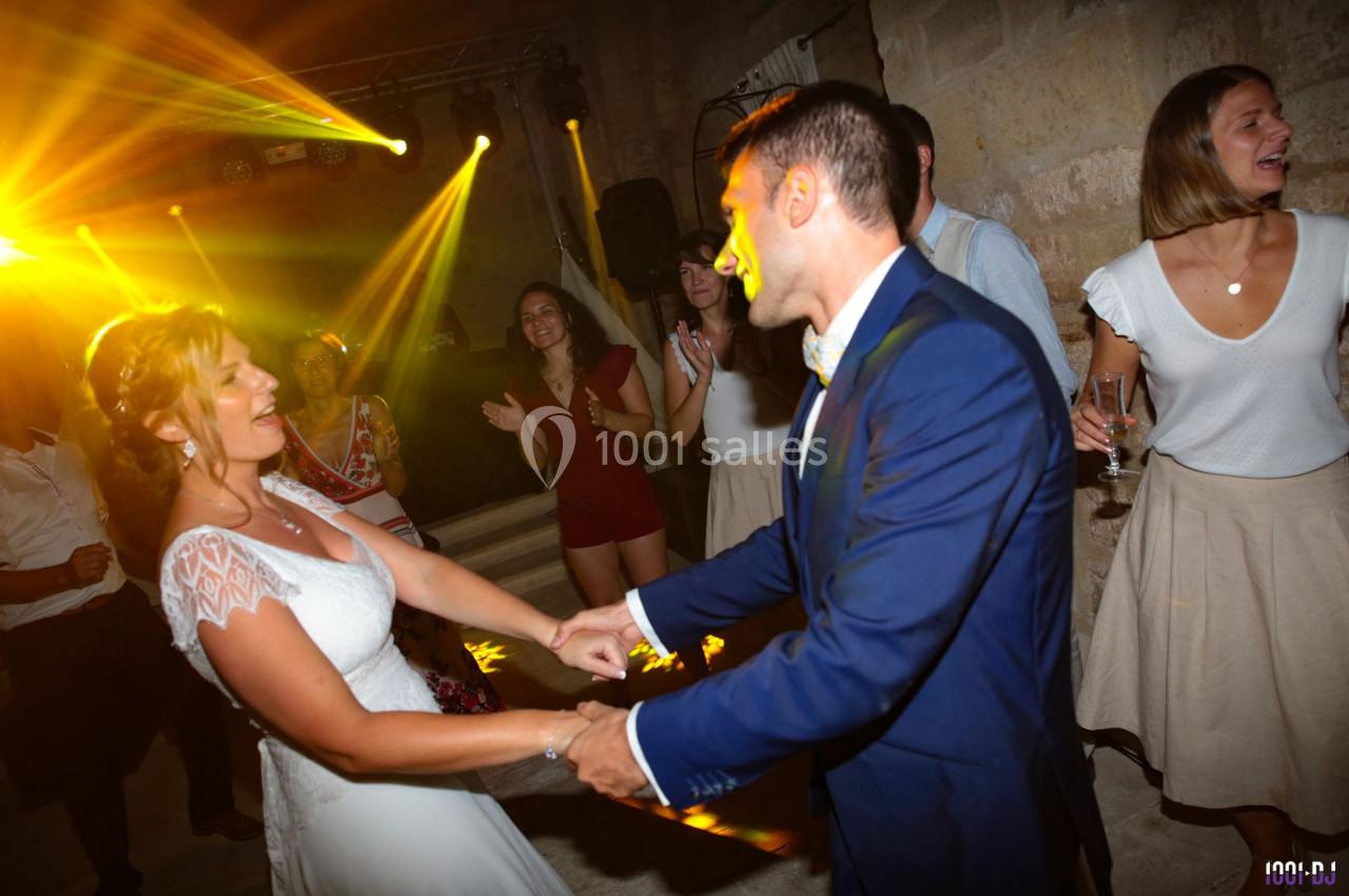 Un couple danse lors d'une fête, entouré d'invités applaudissant sous des lumières colorées.