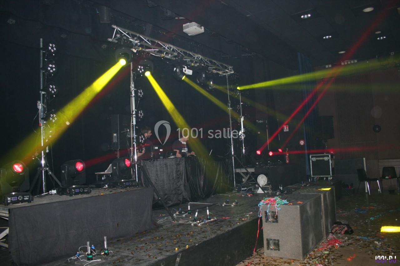 Scène de concert vide avec jeux de lumières colorées, équipement audio et sol jonché de confettis.