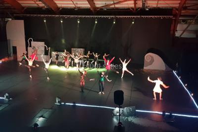 Salle avec éclairage de scène coloré, piste de danse illuminée, tables sur les côtés et matériel audio en arrière-plan.