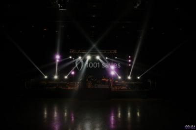 Salle avec éclairage de scène coloré, piste de danse illuminée, tables sur les côtés et matériel audio en arrière-plan.