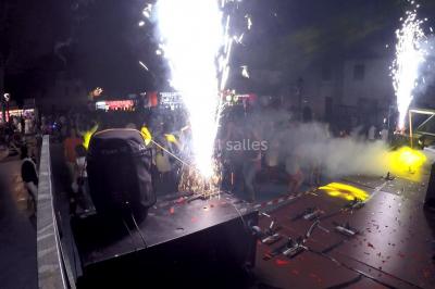 Salle avec éclairage de scène coloré, piste de danse illuminée, tables sur les côtés et matériel audio en arrière-plan.