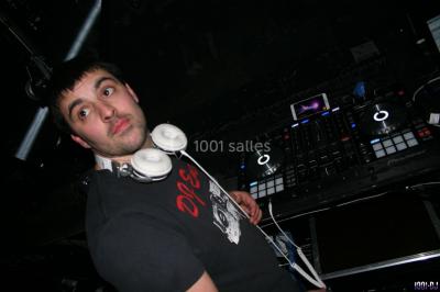 Salle avec éclairage de scène coloré, piste de danse illuminée, tables sur les côtés et matériel audio en arrière-plan.